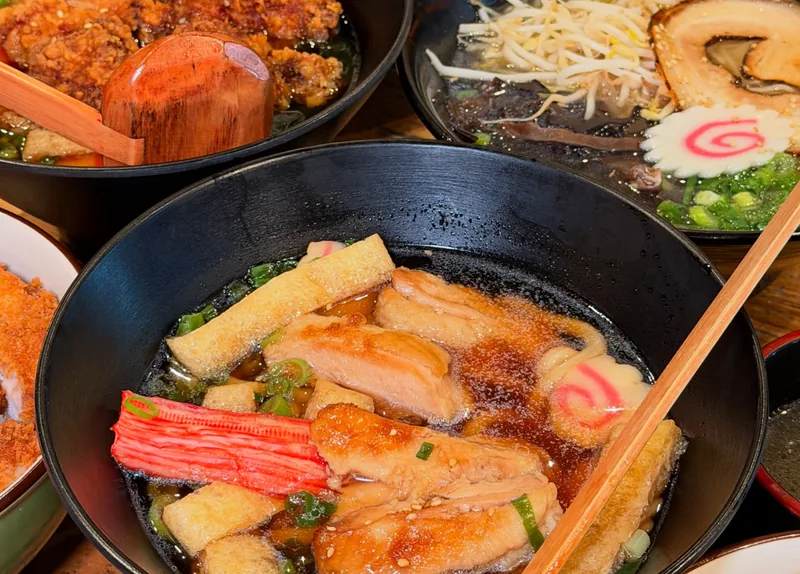 Teriyaki chicken udon, karaage and katsu on a timber table, wooden ladles in the bowls