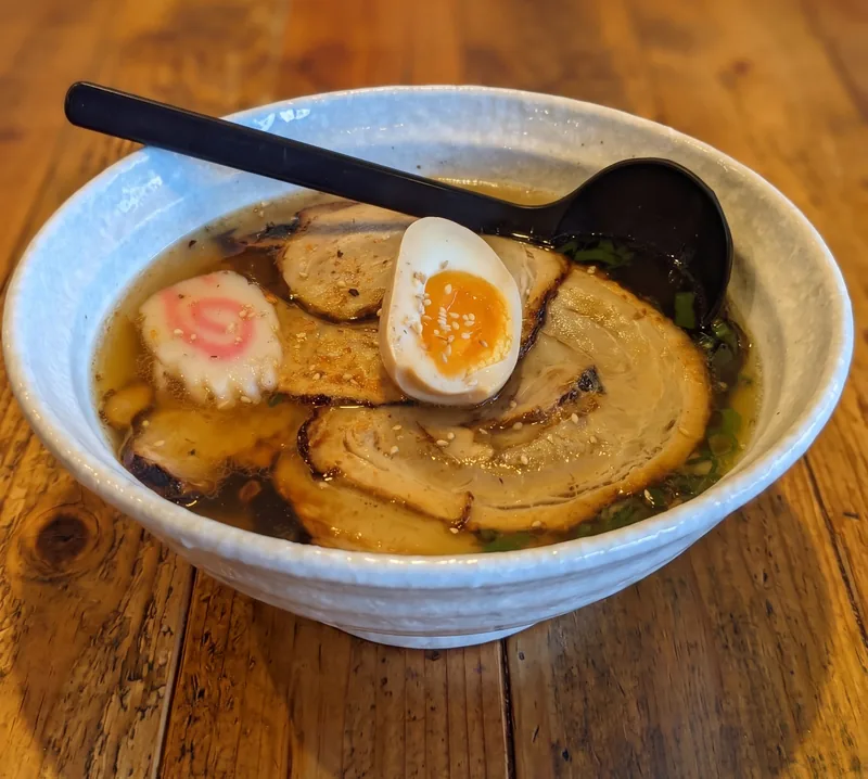 A bowl of soy ramen with chashu, a jammy egg and narutomaki on a timber table