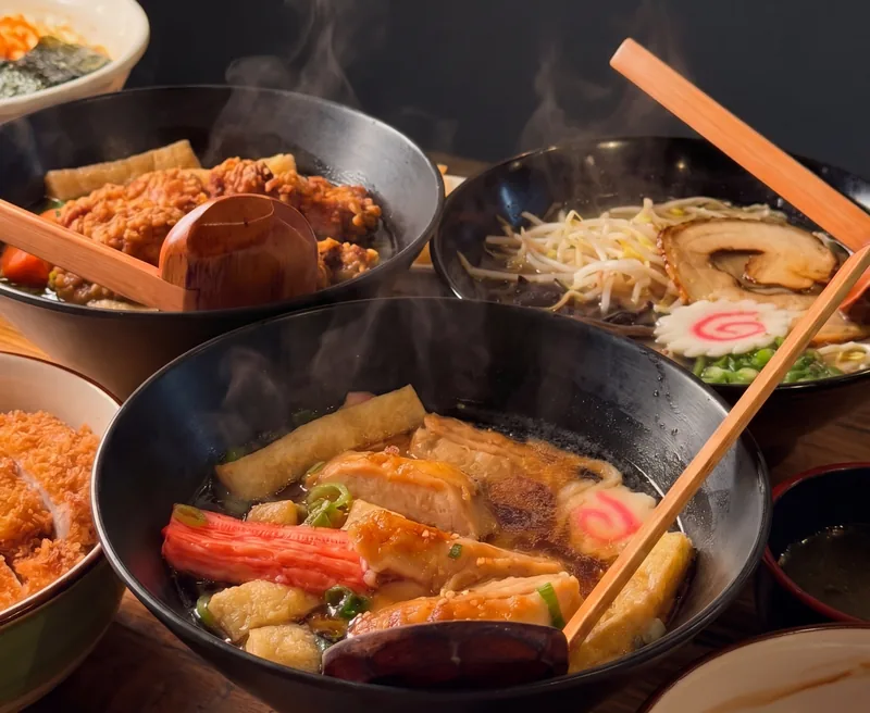 Teriyaki chicken udon, karaage ramen and more on a timber table, wooden ladles in the bowls